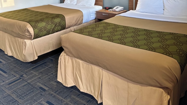 Two single beds with headboards, a bedside table with a lamp, and a telephone. - Budget Host Inn Charleston (Charleston)
