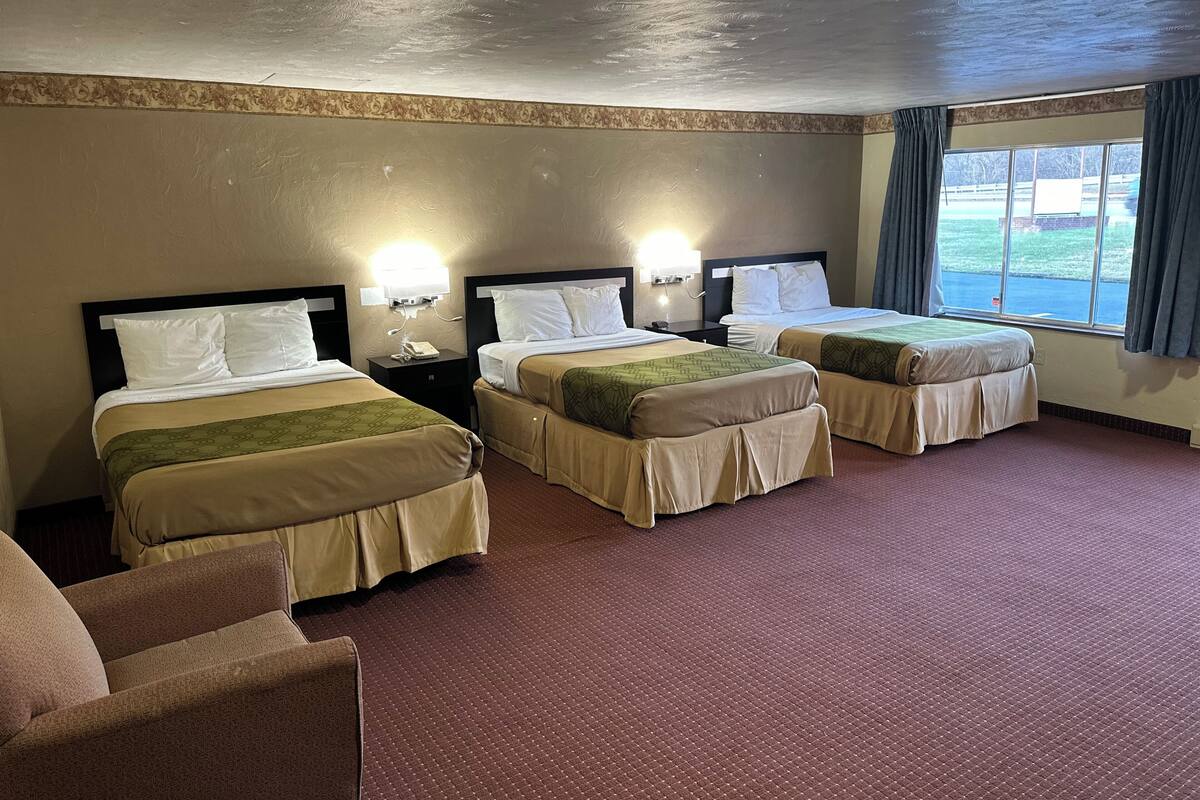 A hotel room with three beds, a desk, and a chair.