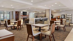 Un comedor de hotel con varias mesas y sillas, una cocina al fondo y una zona de bar.