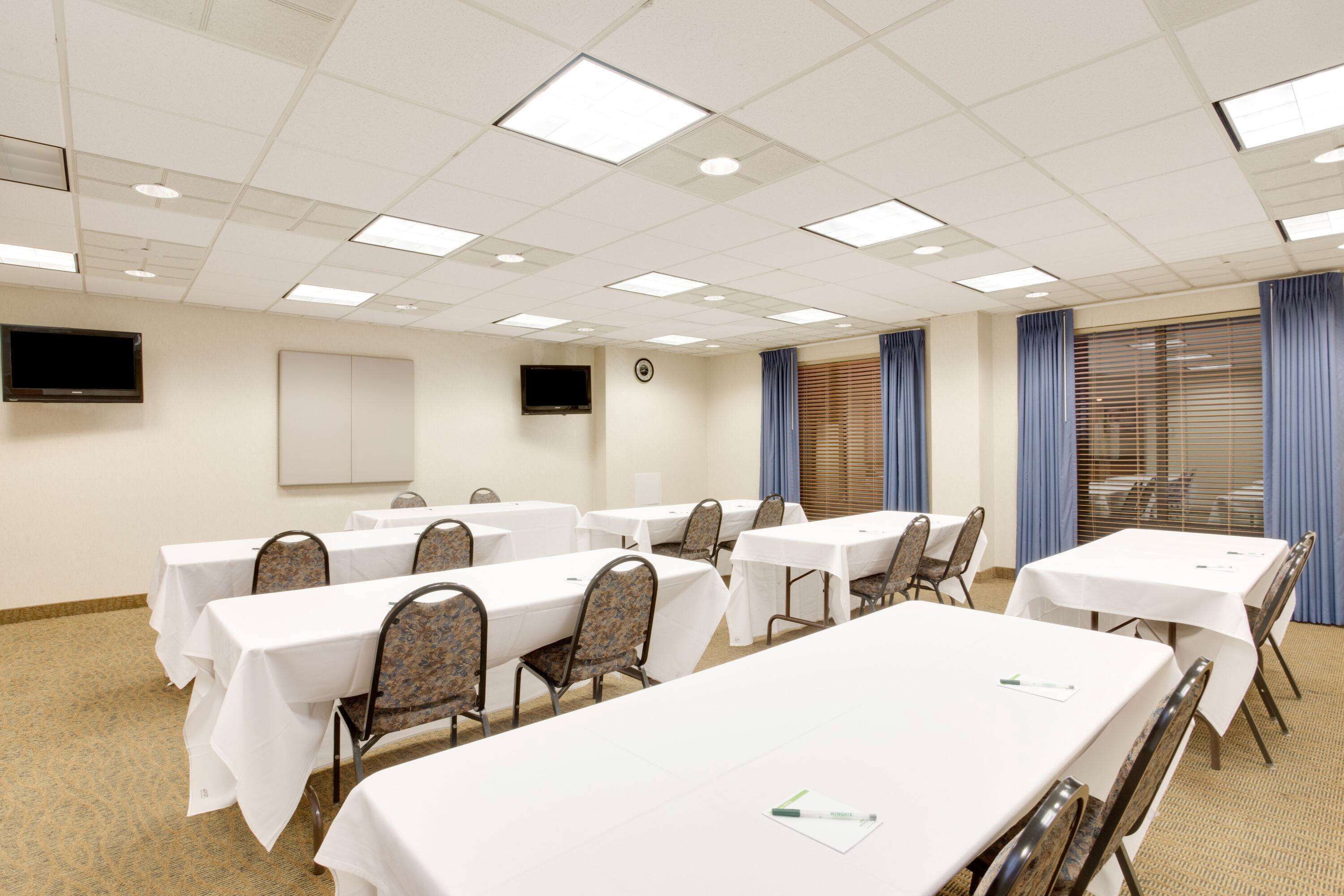 A conference room with multiple tables and chairs, a whiteboard, and a television on the wall.