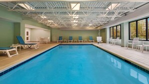 Una piscina interior con suelo de baldosas, sillas de descanso y techo con estructura metálica.