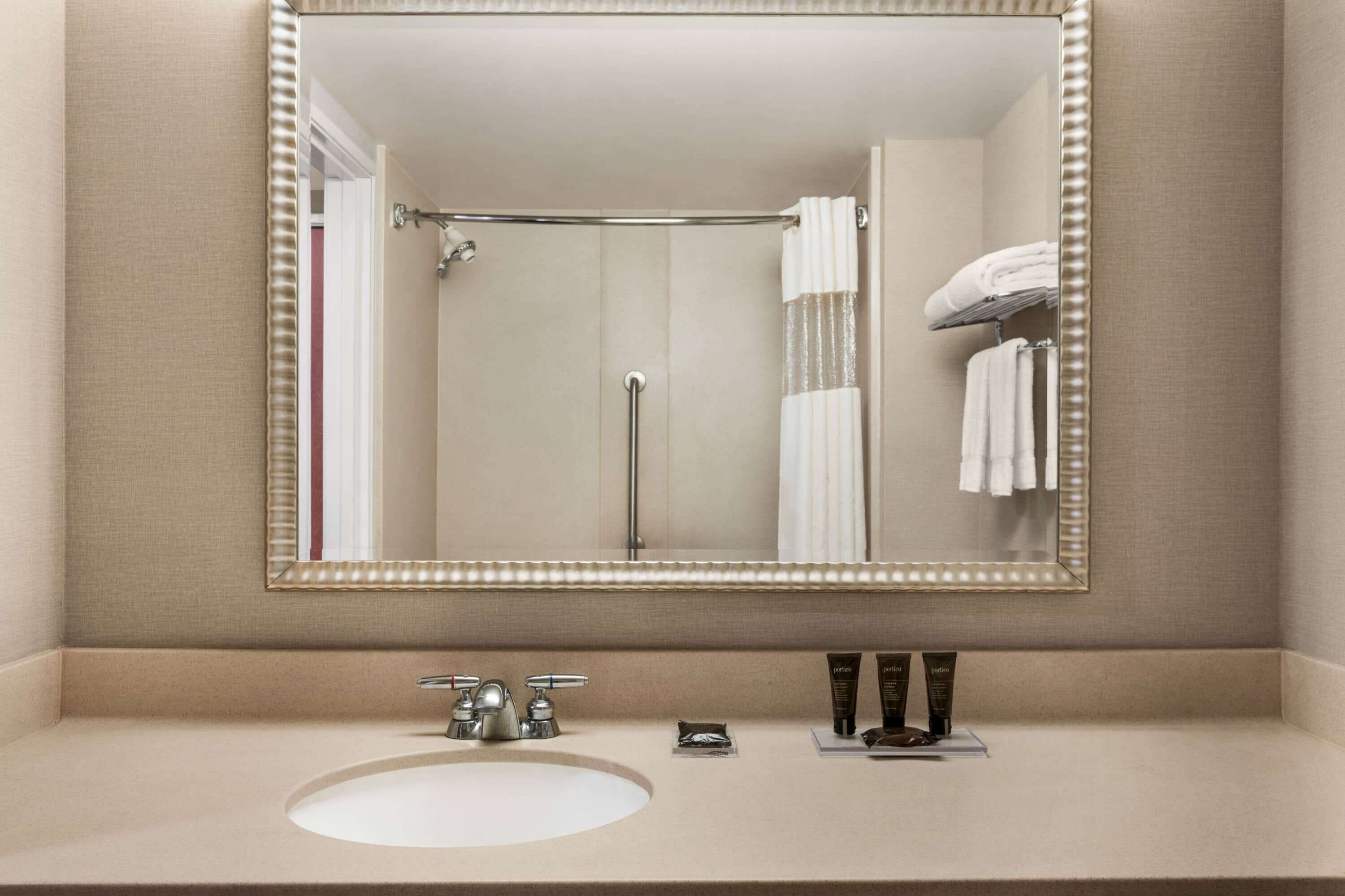 A bathroom with a large mirror, a sink, and a shower area.