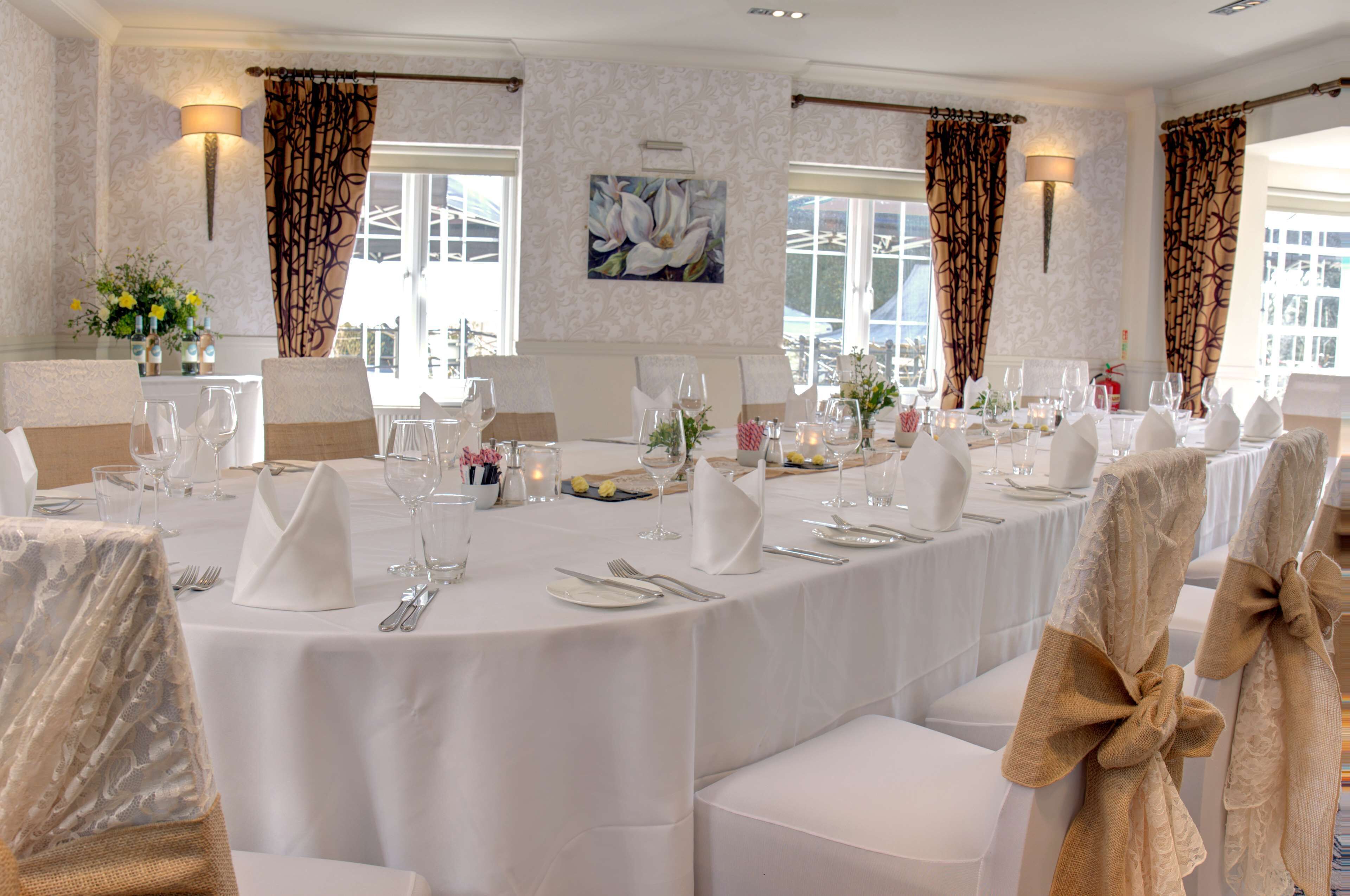 A long dining table set for a formal event, with white tablecloths, neatly arranged silverware, and glassware.