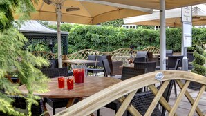 An outdoor seating area with wicker tables and chairs under large umbrellas, surrounded by greenery. - Ivy Hill Hotel, BW Signature Collection (Ingatestone)