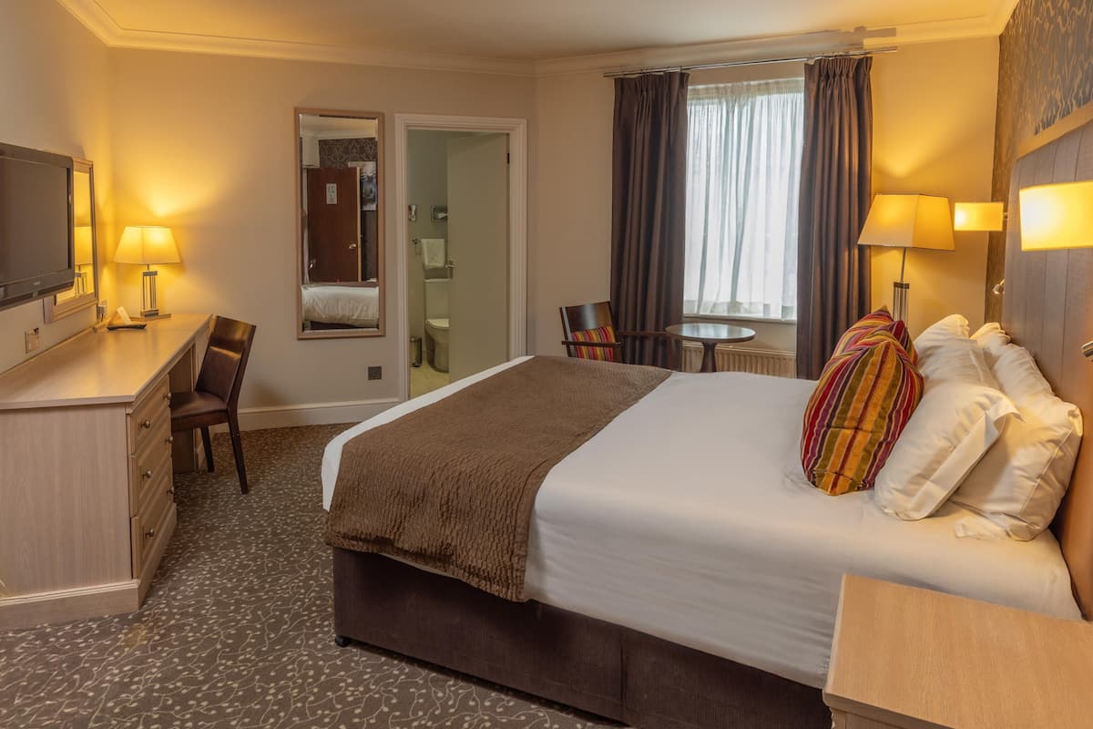 A hotel room with a large bed, a desk with a chair, a TV, and a small table with a chair.