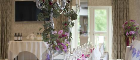 Una mesa de banquete decorada con manteles blancos, candelabros de plata y flores moradas.