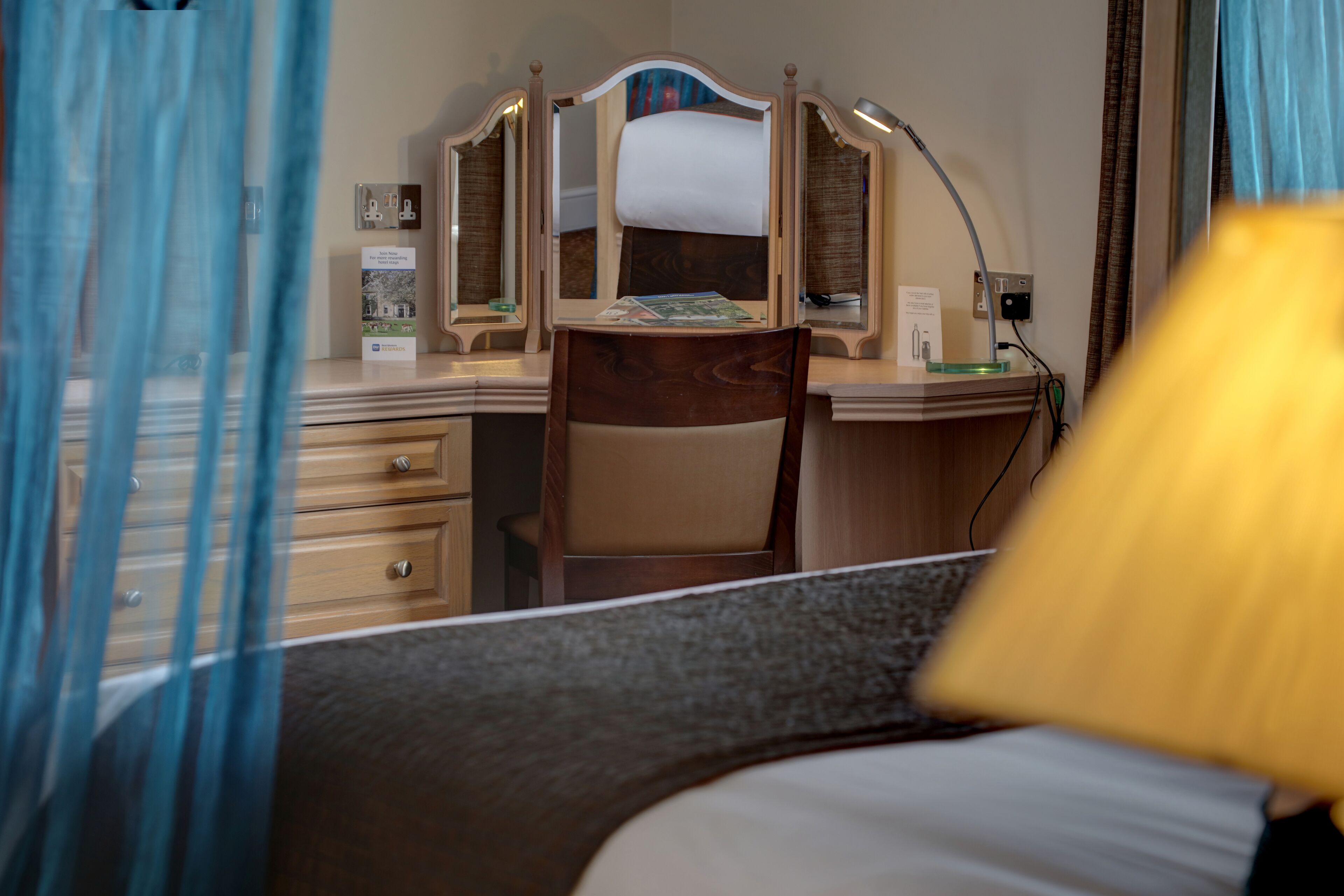 Et hotelværelse med seng, skrivebord med stol, spejl og lampe.