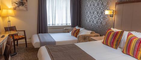 Une chambre d’hôtel avec deux lits, un bureau, une chaise, une lampe et une fenêtre avec des rideaux.