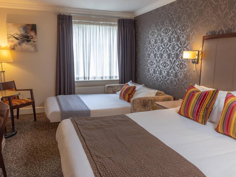 Une chambre d’hôtel avec deux lits, un bureau, une chaise, une lampe et une fenêtre avec des rideaux.