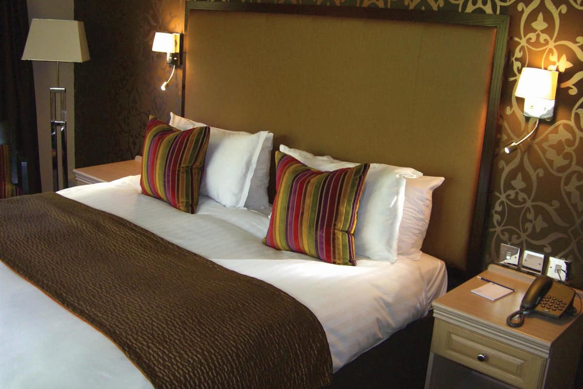 A hotel room with a large bed, two bedside lamps, a nightstand with a telephone, and a patterned wall.