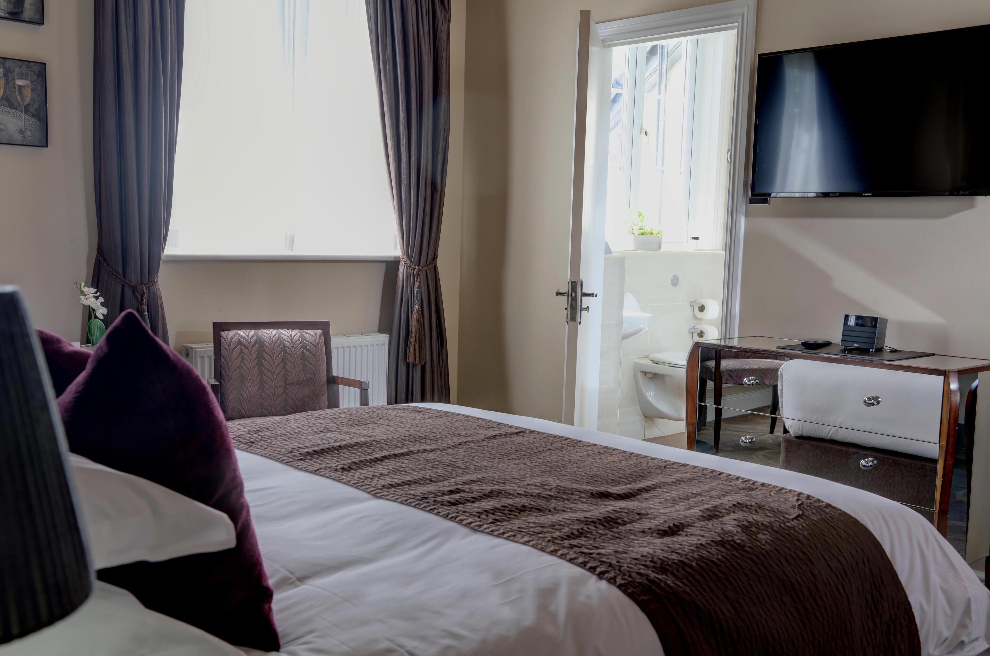 A hotel room with a bed, a desk, a TV, and a bathroom visible through an open door.