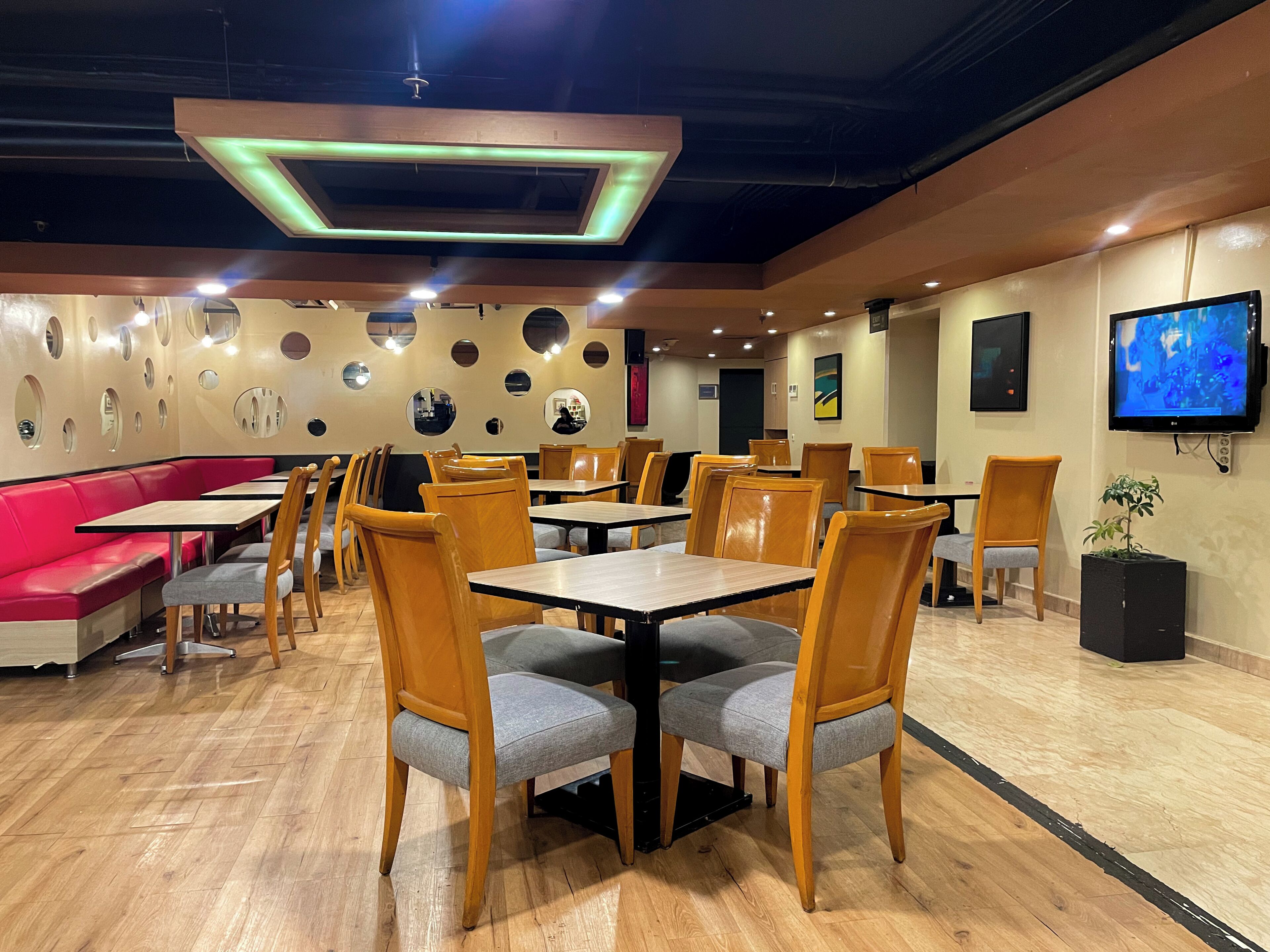 A restaurant interior with round tables, wooden chairs, a red booth, and a TV on the wall.