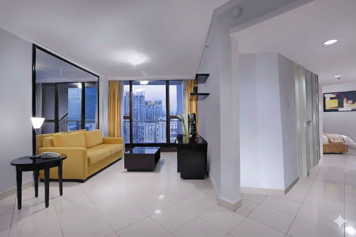 A modern living room with a yellow sofa, a black coffee table, and a view of tall buildings through large windows.