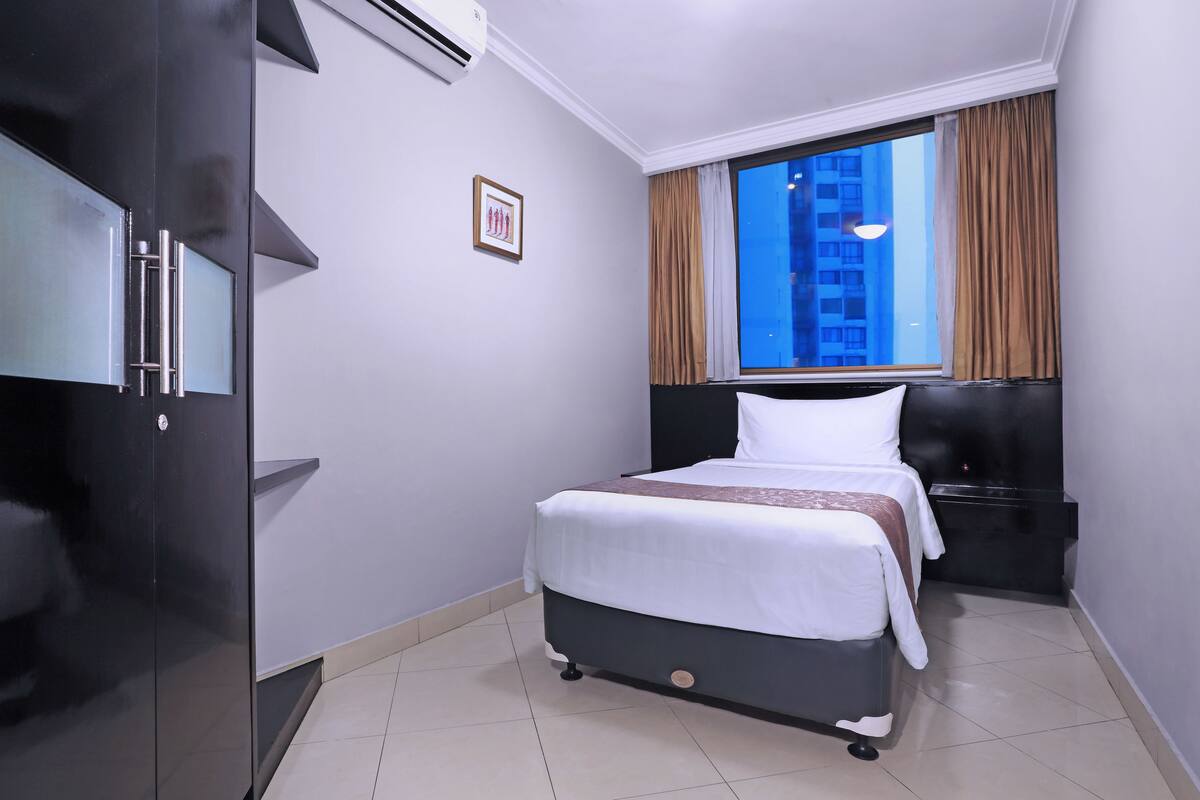 A hotel room with a bed, a wardrobe, a window with curtains, and a framed picture on the wall.