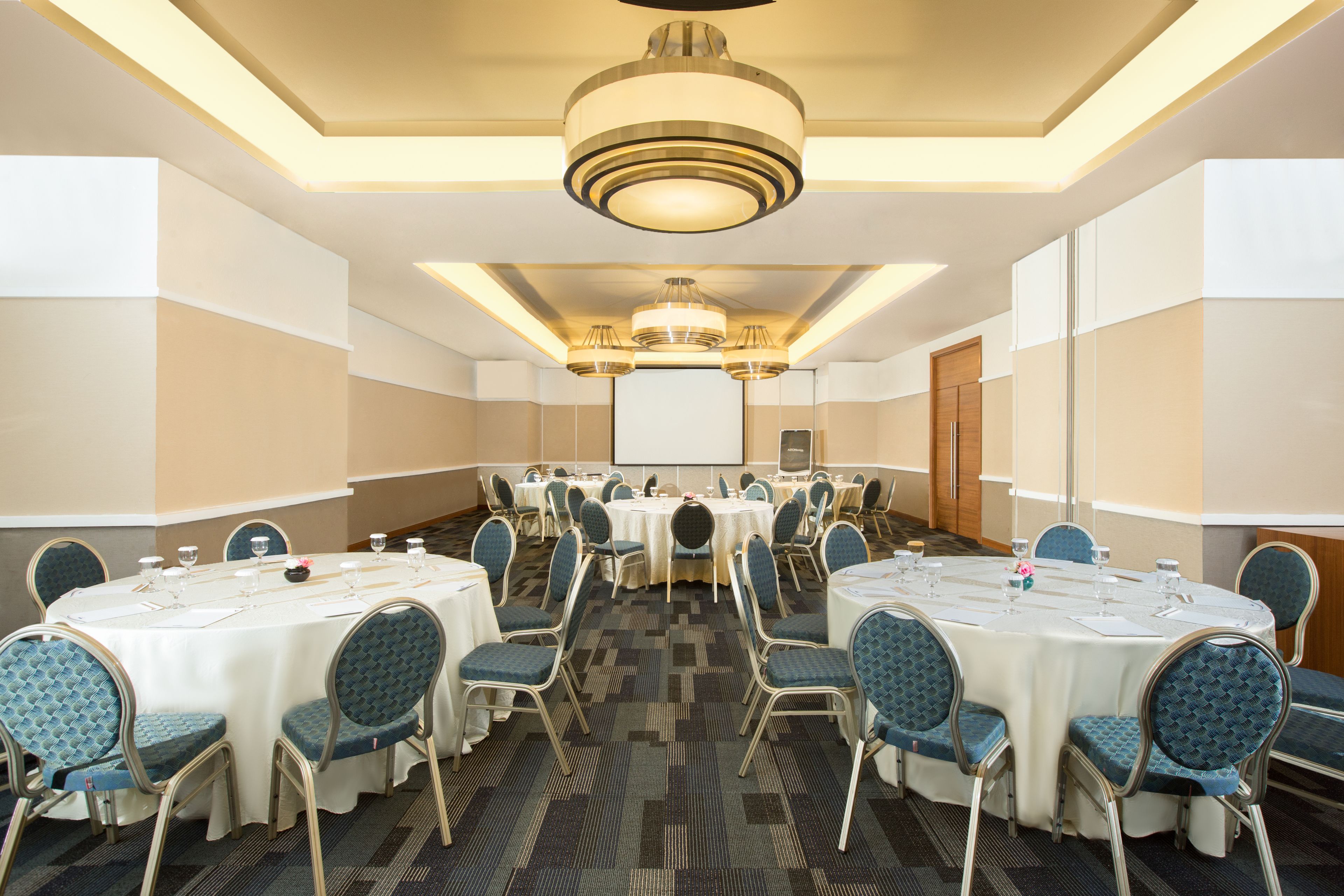 A conference room with round tables, chairs, and a projector screen.