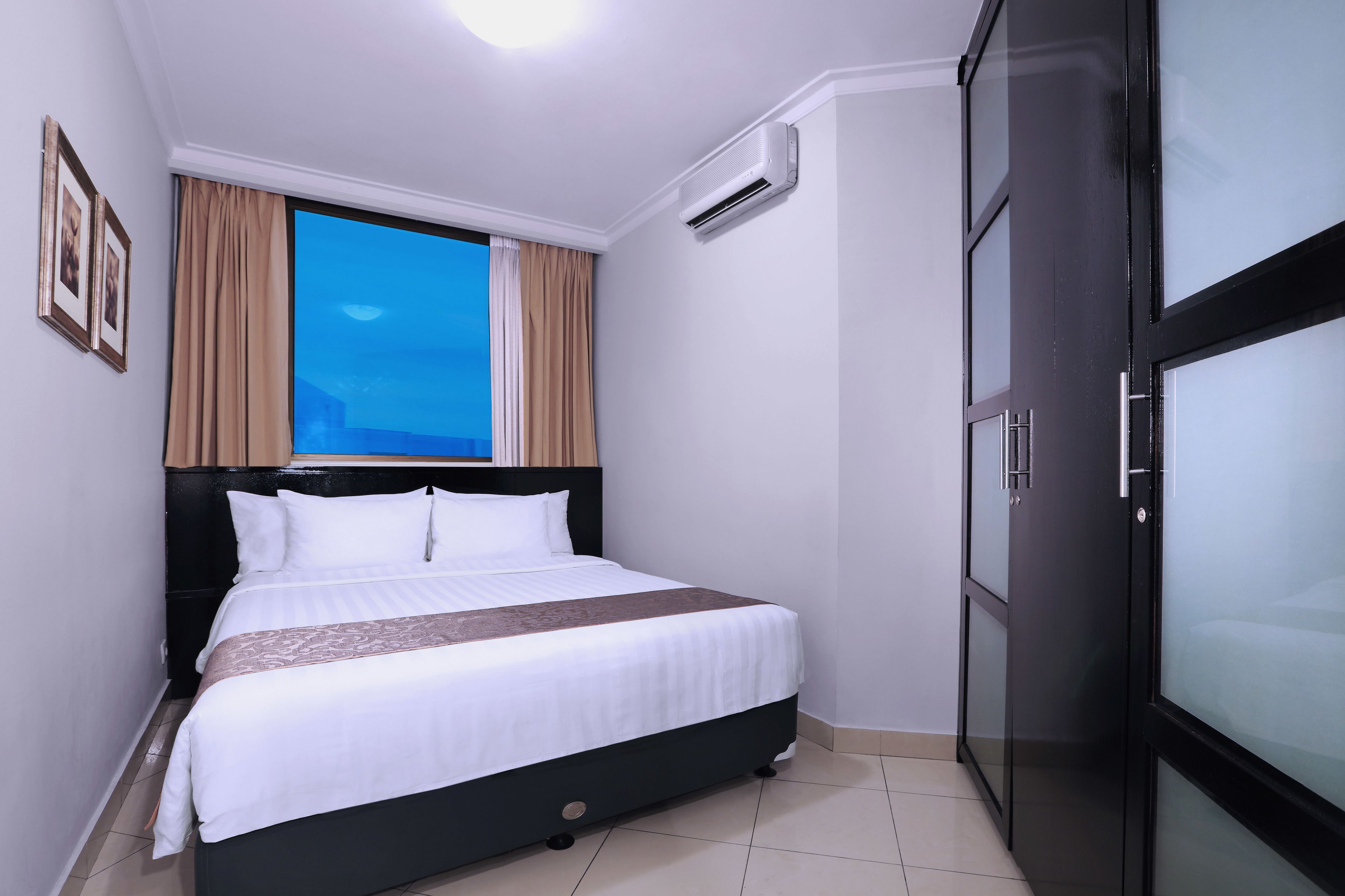 A neatly made bed with a white and brown bedspread, a black headboard, and a window with beige curtains.