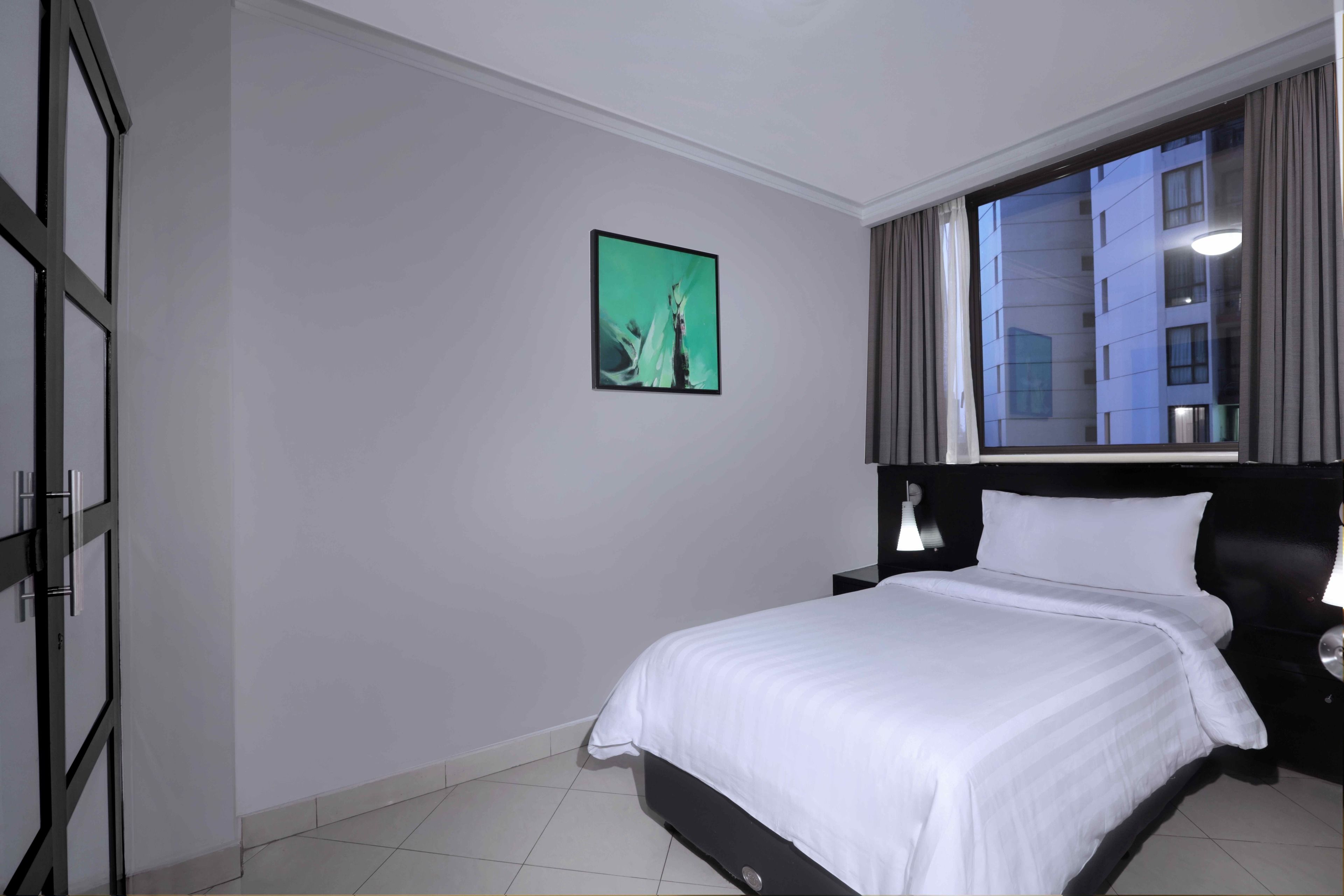 Ein Hotelzimmer mit einem Bett, einem Nachttisch, einem Wandbild und einem Fenster mit Vorhängen.