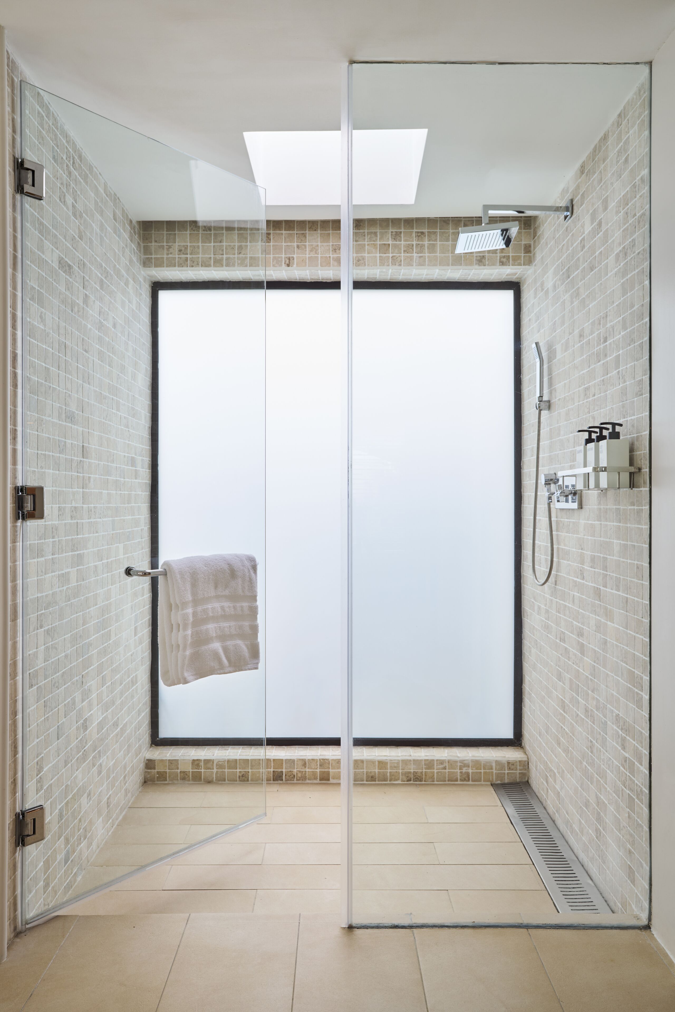 A modern bathroom with a glass door, a shower, and a towel hanging on the door handle.