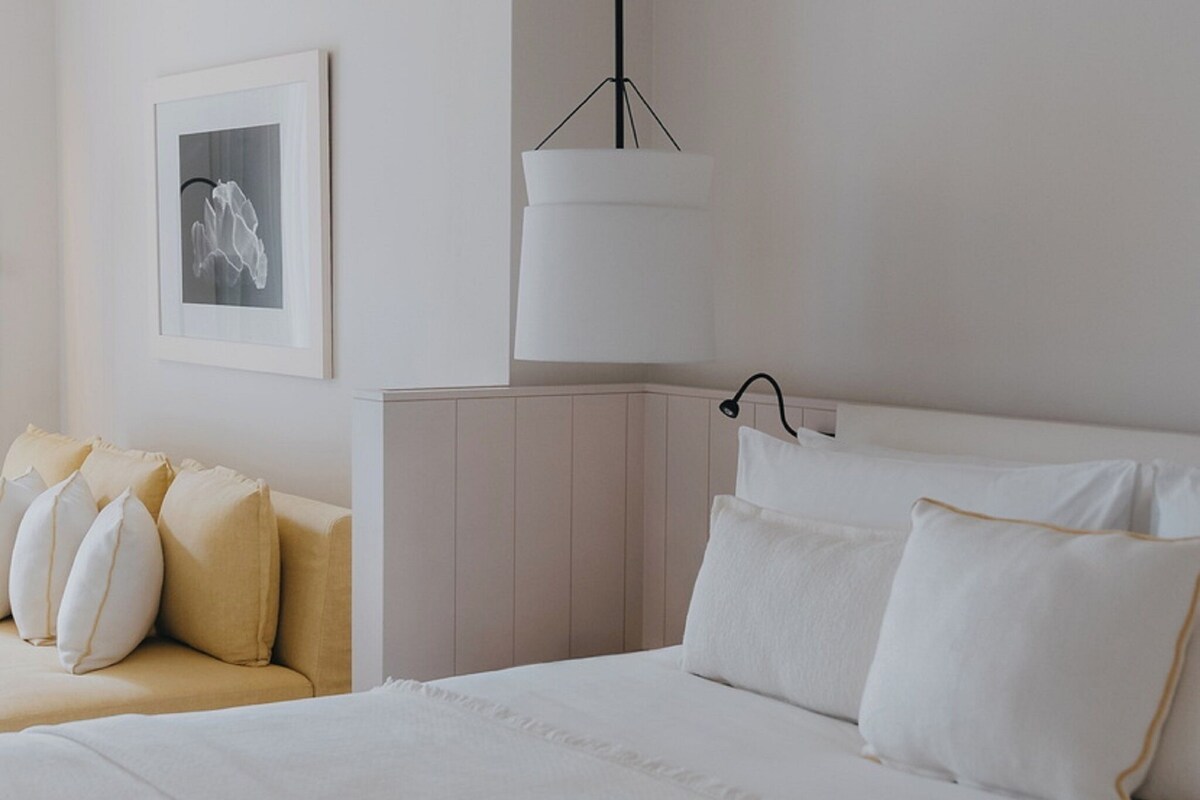 Een slaapkamer met een groot bed, een nachtkastje, een hanglamp en een lijst met een afbeelding aan de muur.