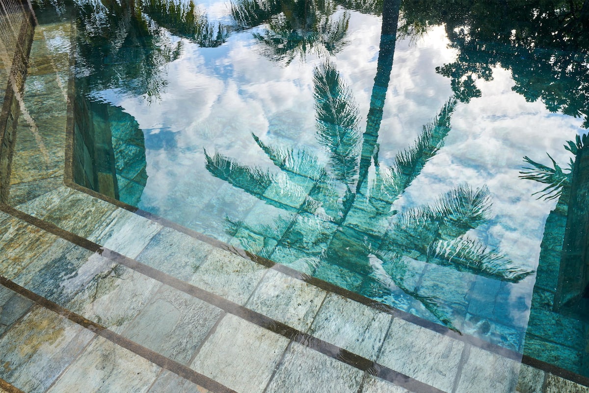 Una piscina nítida amb reflexos de palmeres i un cel nuvolós.