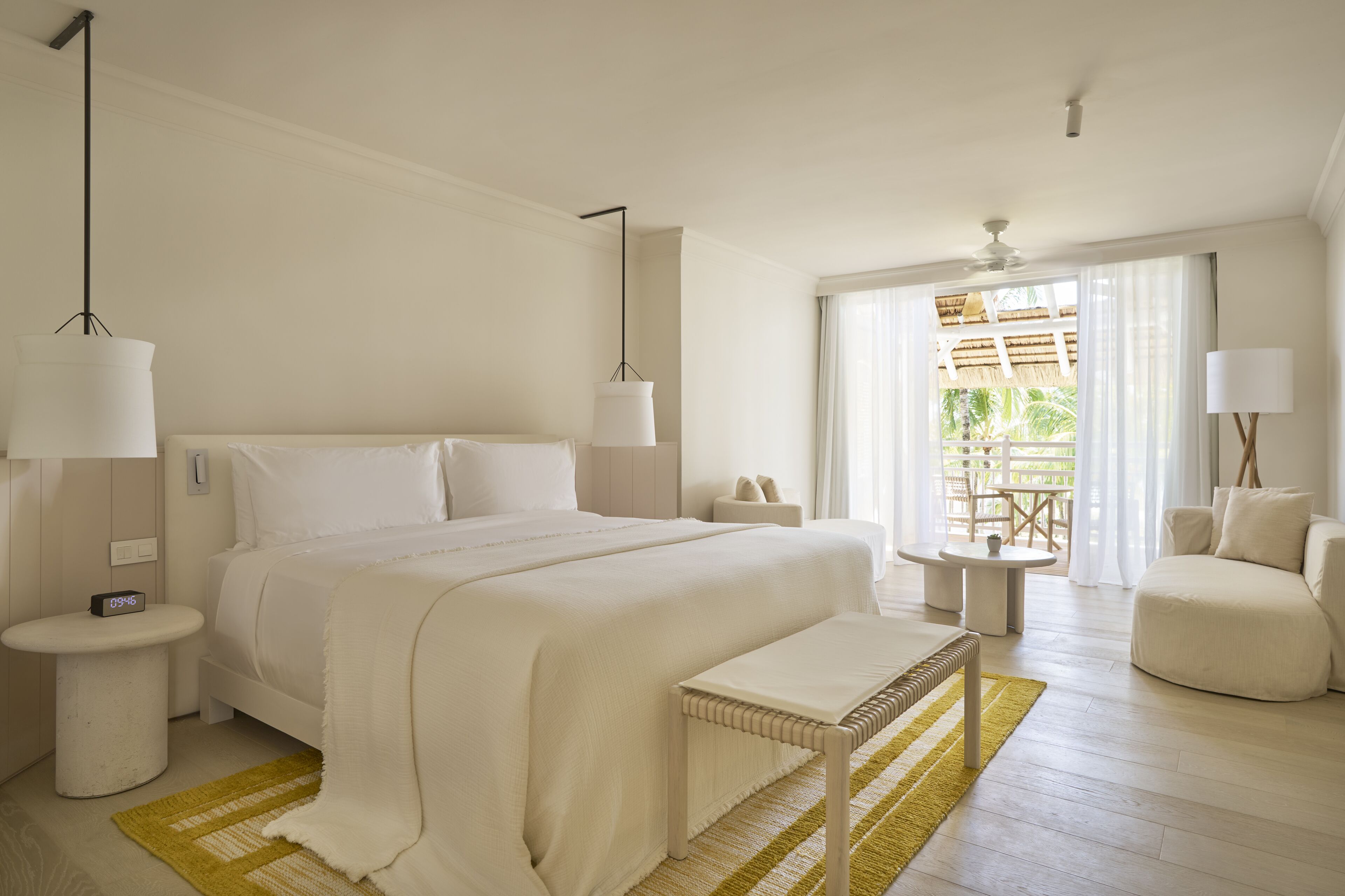 A spacious bedroom with a large bed, bedside tables, a bench, and a view of an outdoor area with a table and chairs.