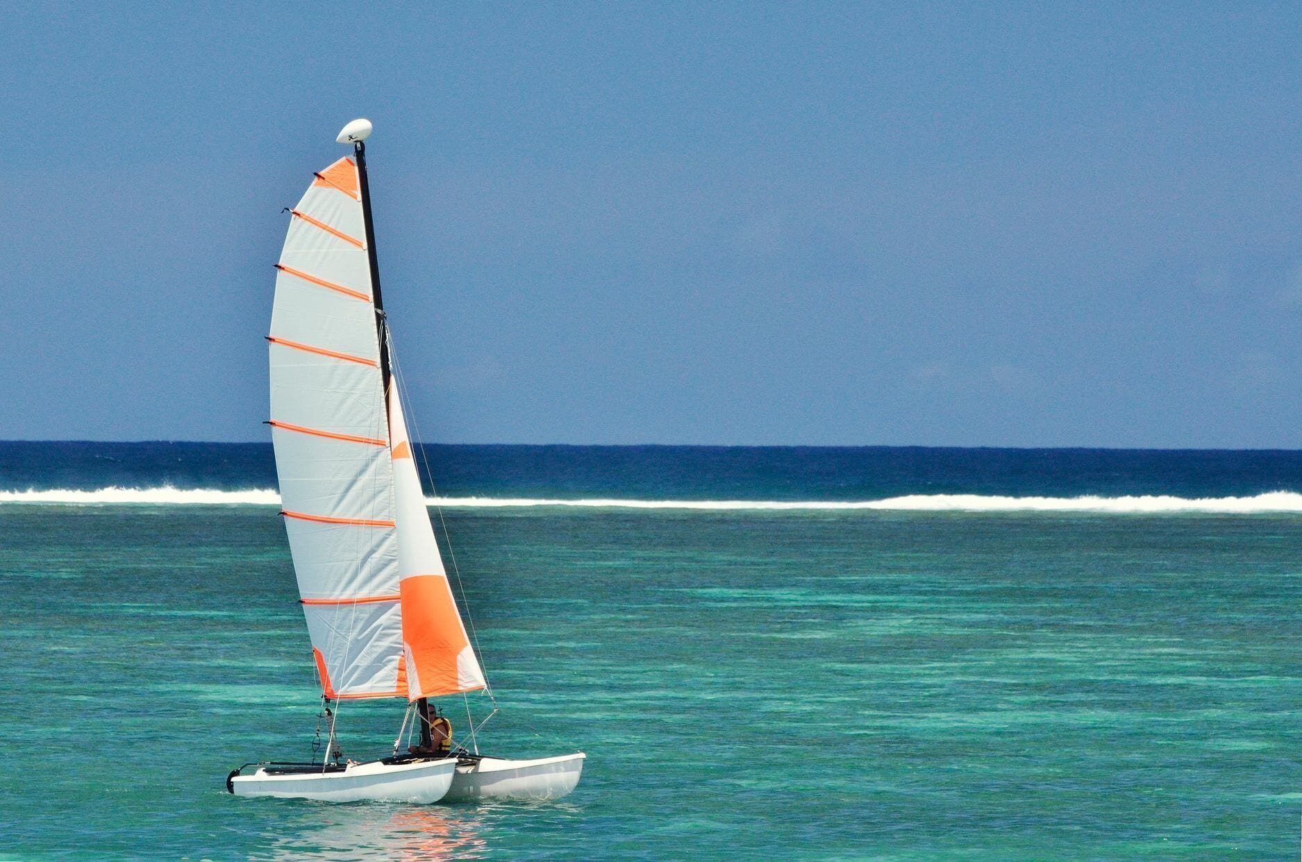 Un velero con una sola vela en aguas turquesas tranquilas.