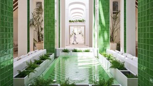 Un área de piscina interior moderna con paredes de azulejos verdes, asientos blancos y plantas en macetas.