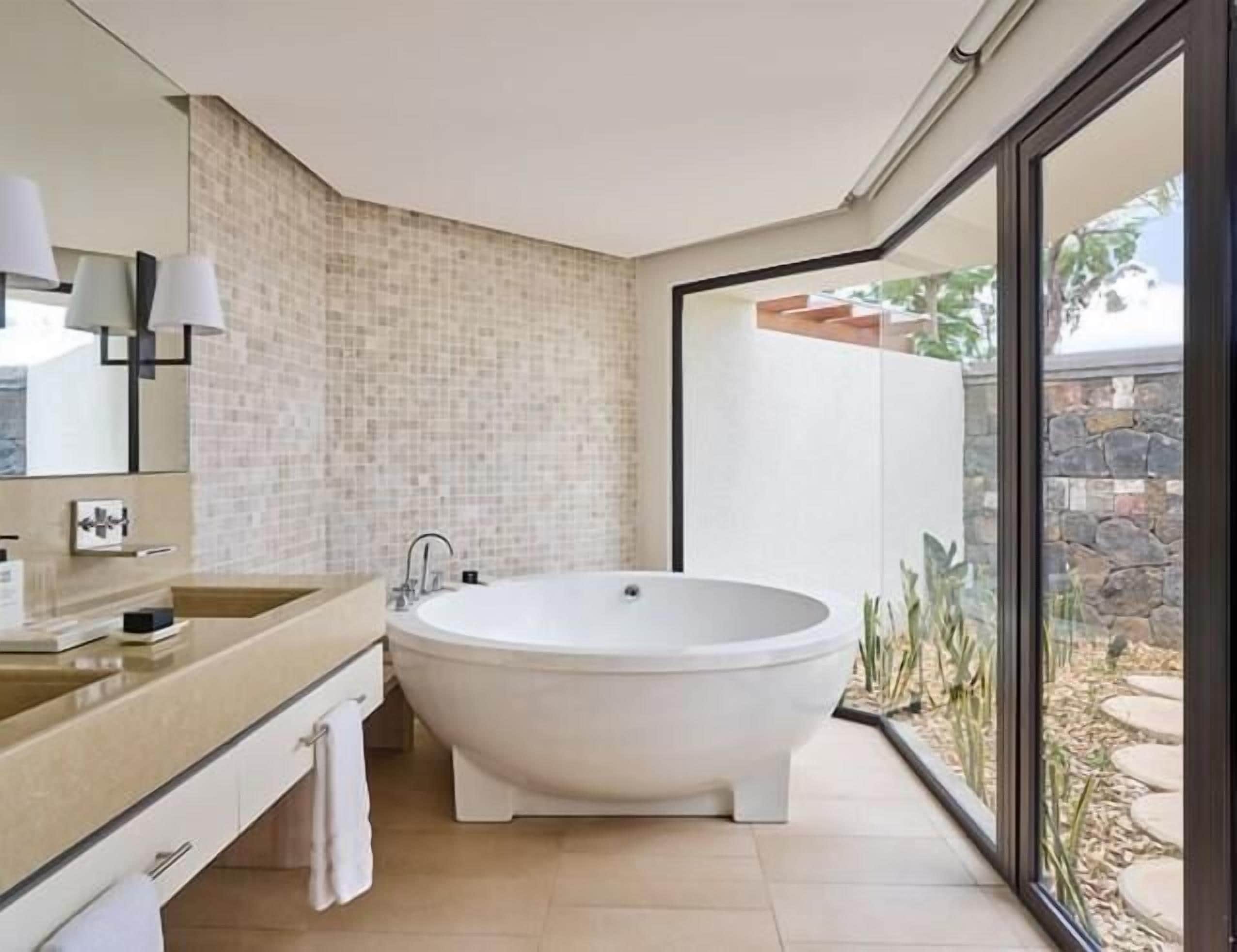 Een moderne badkamer met een vrijstaand bad, een grote spiegel en uitzicht op de natuur.