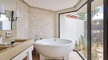 Een moderne badkamer met een vrijstaand bad, een grote spiegel en uitzicht op de natuur.