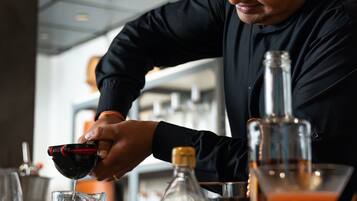 Un bartender preparando una bebida con un agitador, una copa de martini y una botella de licor sobre una barra.