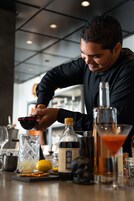 Un bartender preparando una bebida con un agitador, una copa de martini y una botella de licor sobre una barra.