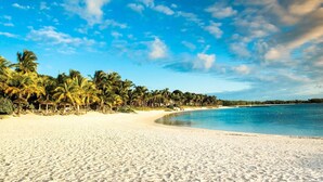 Una playa con arena blanca, palmeras y un cielo azul despejado.