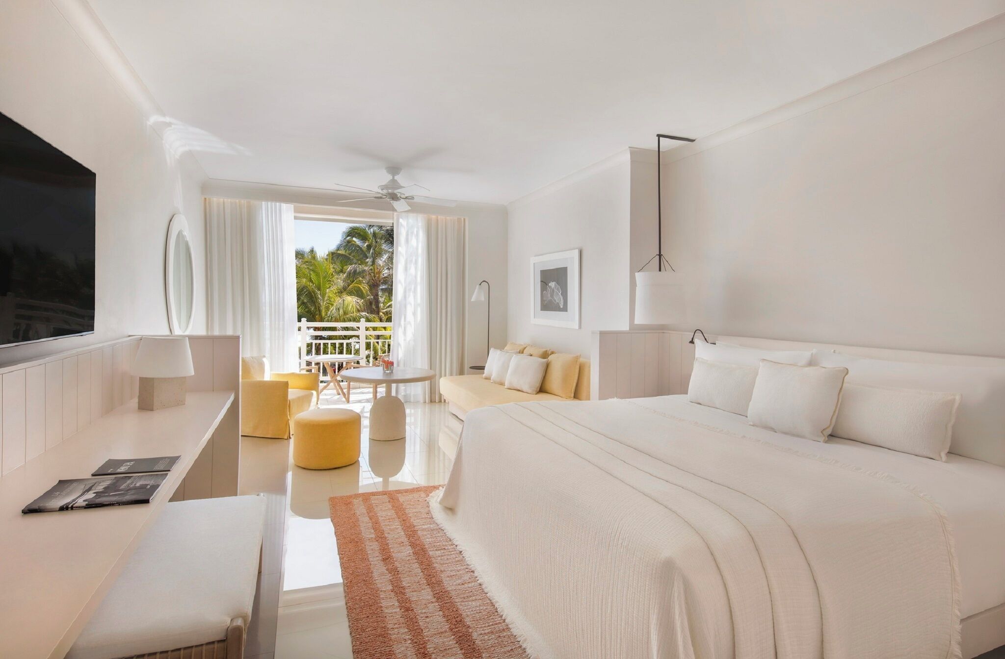 A modern hotel room with a large bed, a desk, and a balcony with a view of palm trees.