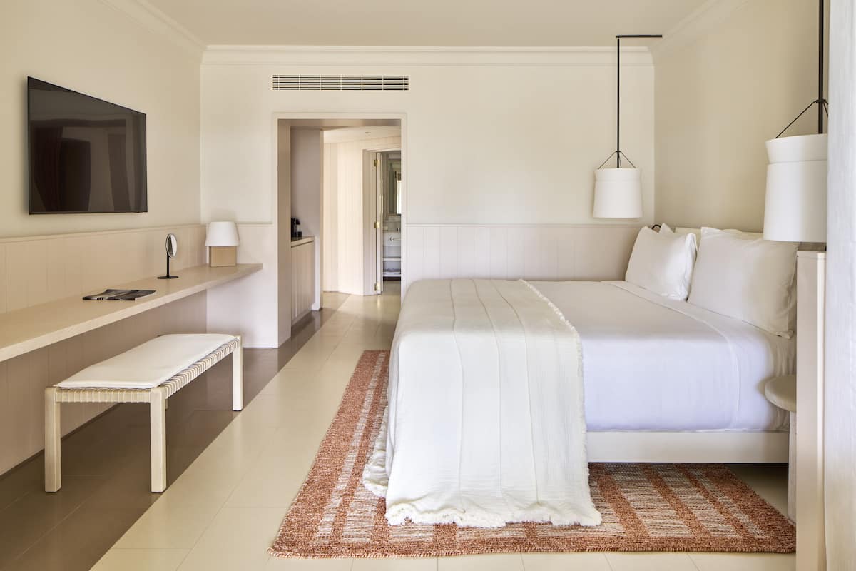 Habitació d'hotel moderna amb un llit gran, una banca, una televisió i una làmpada.