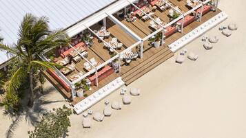 An aerial view of a beachside resort with multiple seating areas, including white and red sofas, and a variety of tables and chairs.