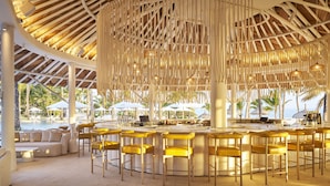 Zona de bar con taburetes amarillos, una piscina al fondo y un entorno tropical con palmeras.