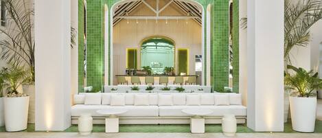 Un hall d’entrée moderne avec un canapé blanc, deux tables rondes et un mur recouvert de carreaux verts.