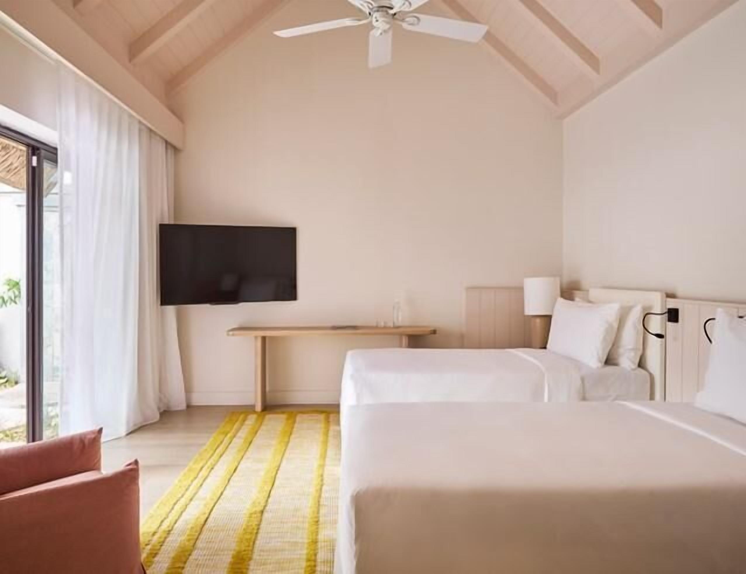 Habitación de hotel con dos camas, televisión, escritorio y ventana con cortinas.