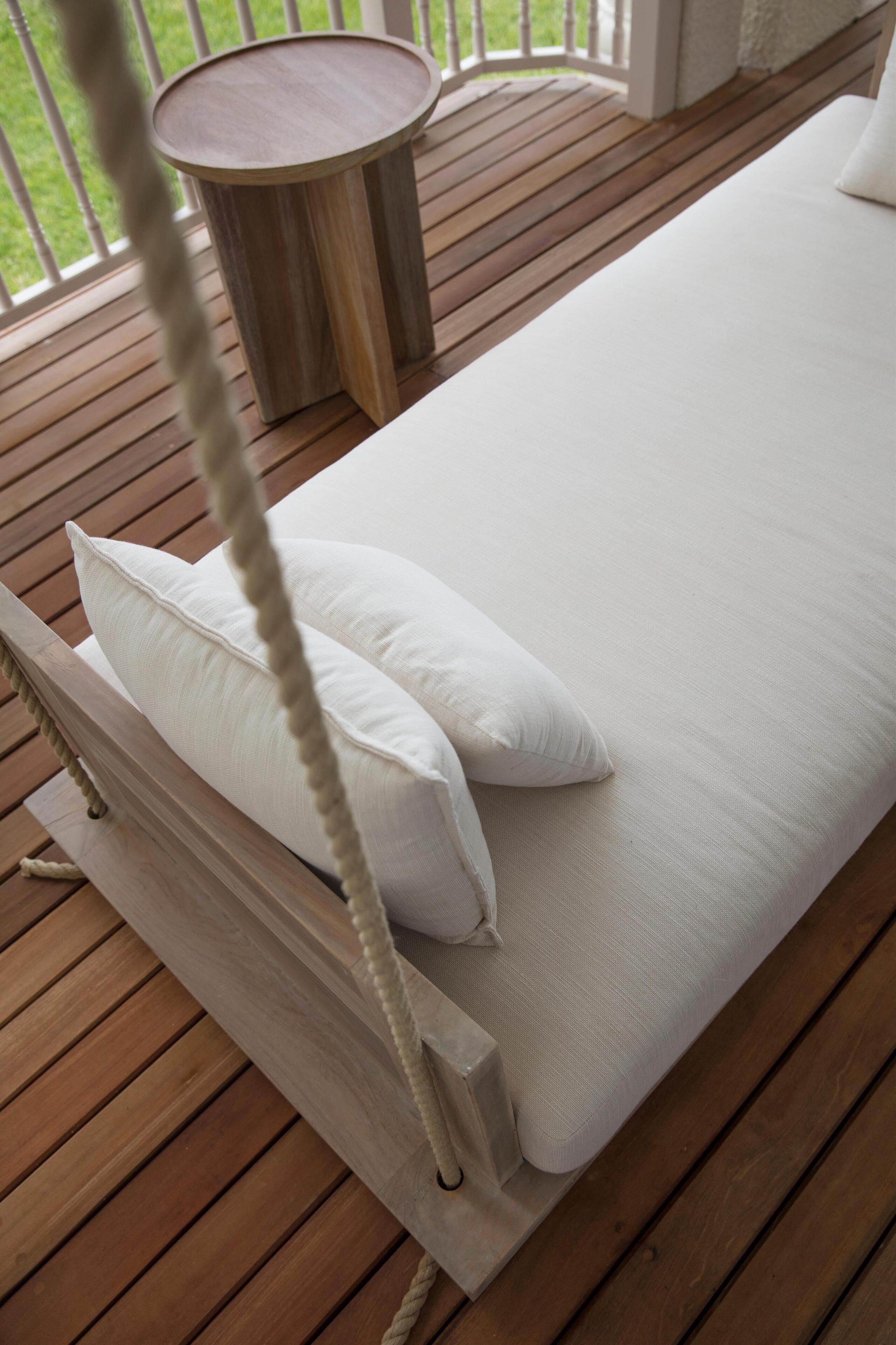 A wooden deck with a white cushioned bench and a round table.
