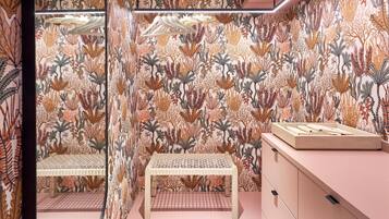 Un baño con papel tapiz estampado, una banca y un tocador con cajones.