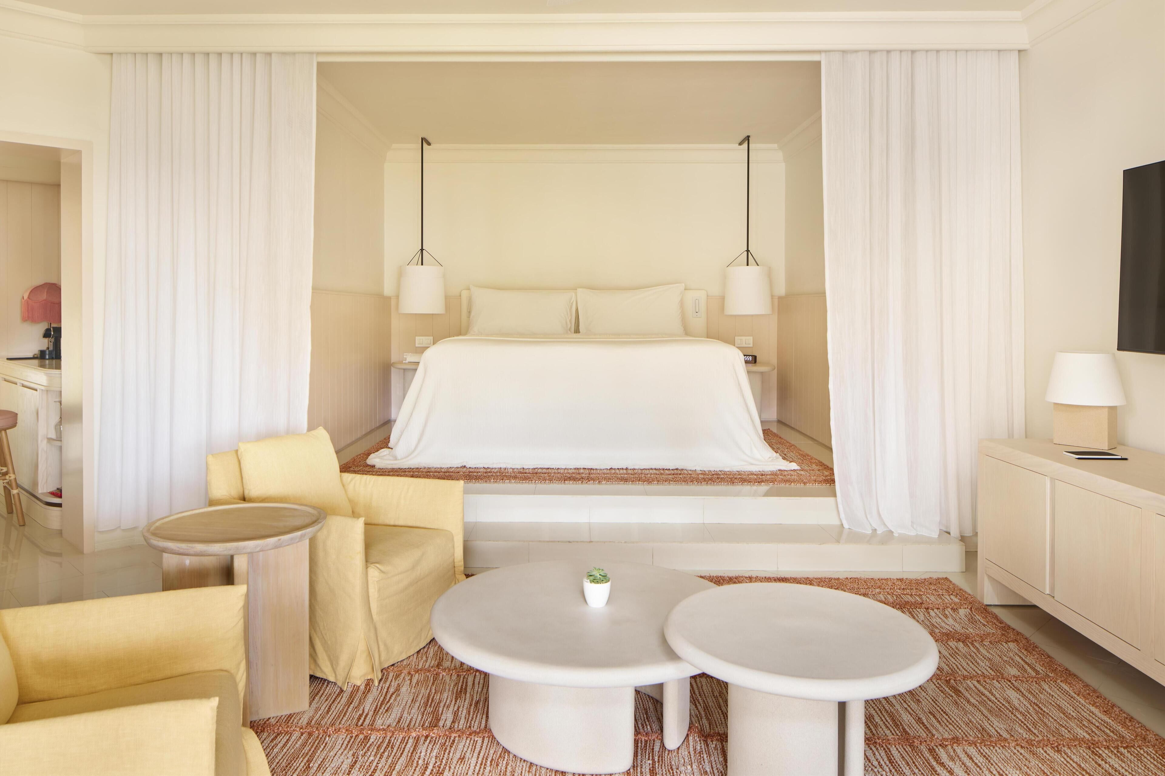 A hotel room with a large bed, two bedside tables, a small round table, a sofa, and a TV.