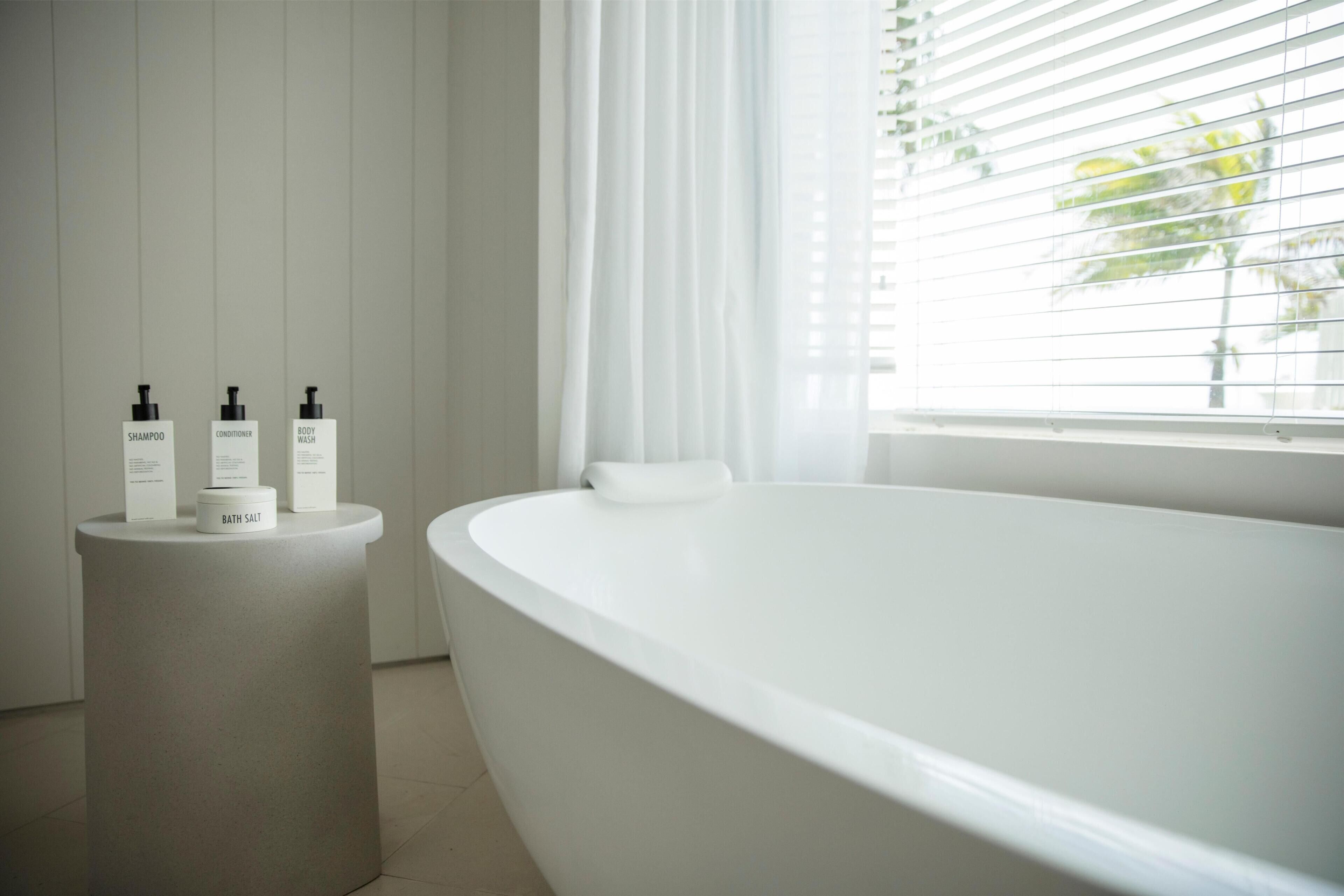 Et moderne badeværelse med et fristående badekar, en rund vask med toiletartikler og et vindue med skodder.