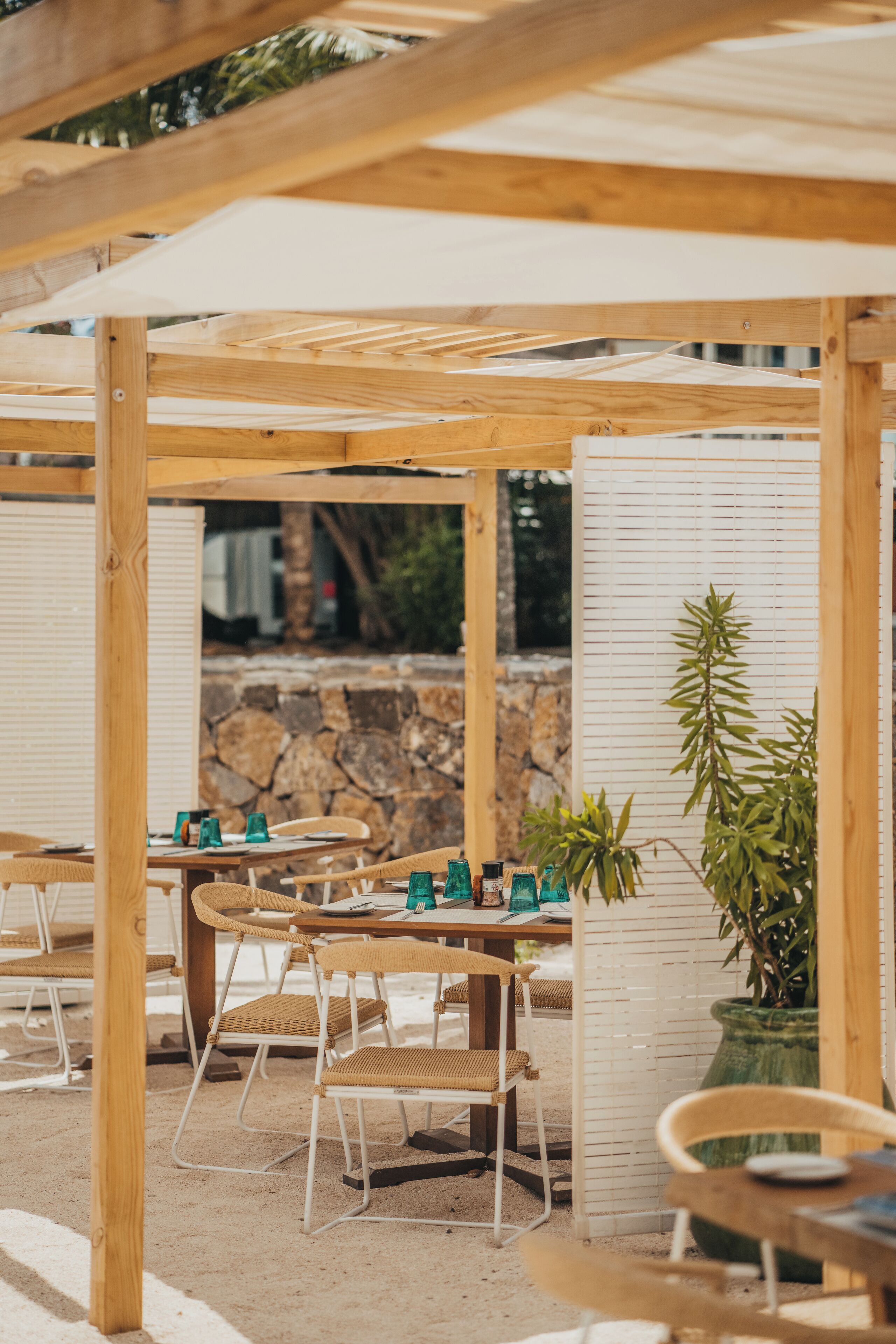 An outdoor seating area with wooden tables and chairs, surrounded by a wooden pergola.