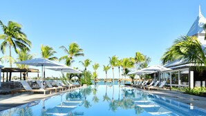 Un espace piscine agrémenté de chaises longues et de parasols, entouré de palmiers.