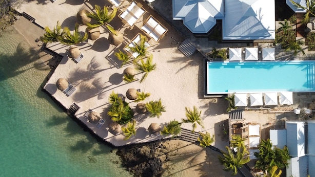 Vue aérienne d’un complexe hôtelier avec une piscine, des chaises longues et des palmiers.