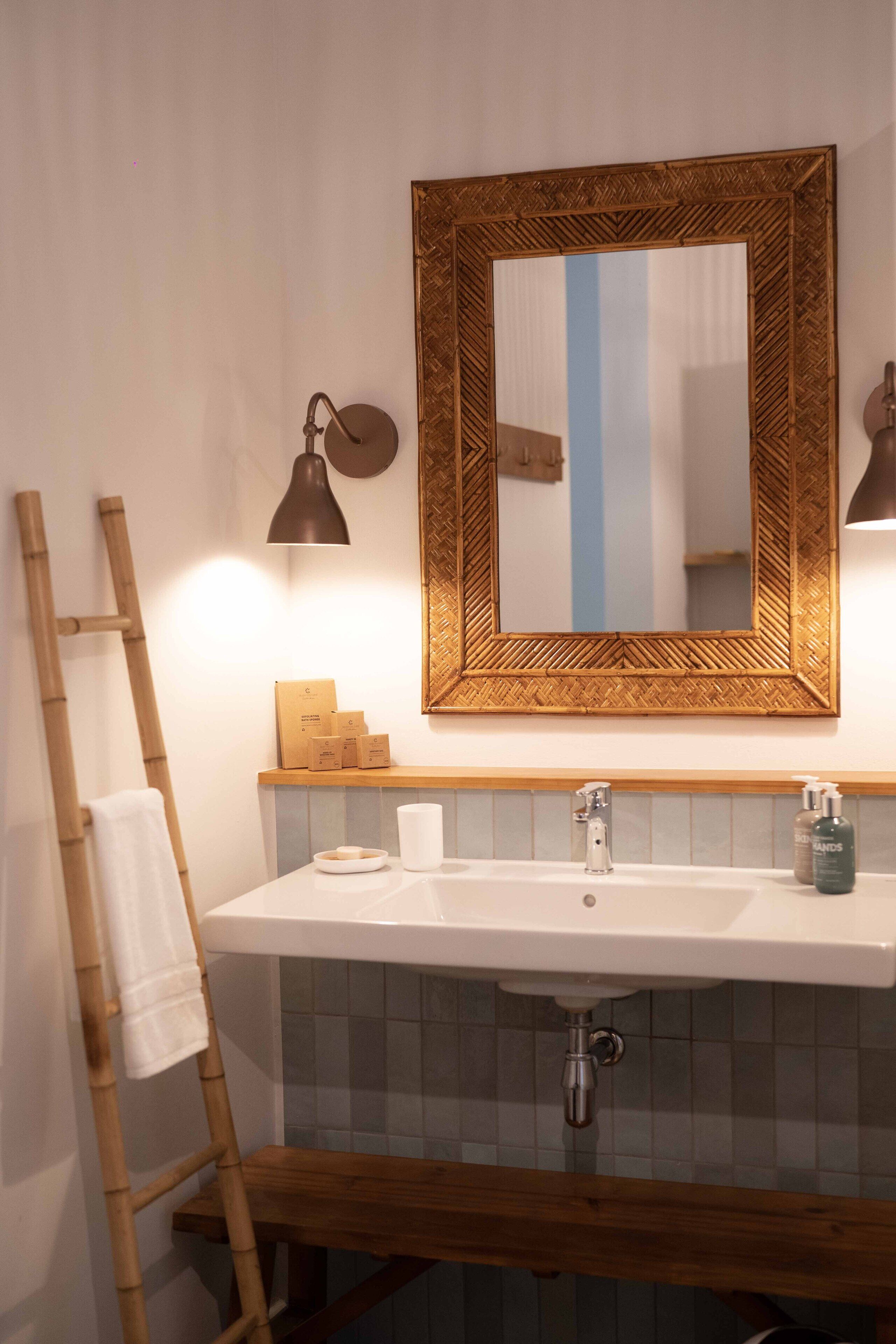 A bathroom with a wooden ladder, a large mirror, a sink with a soap dispenser, and a towel hanging on the wall.