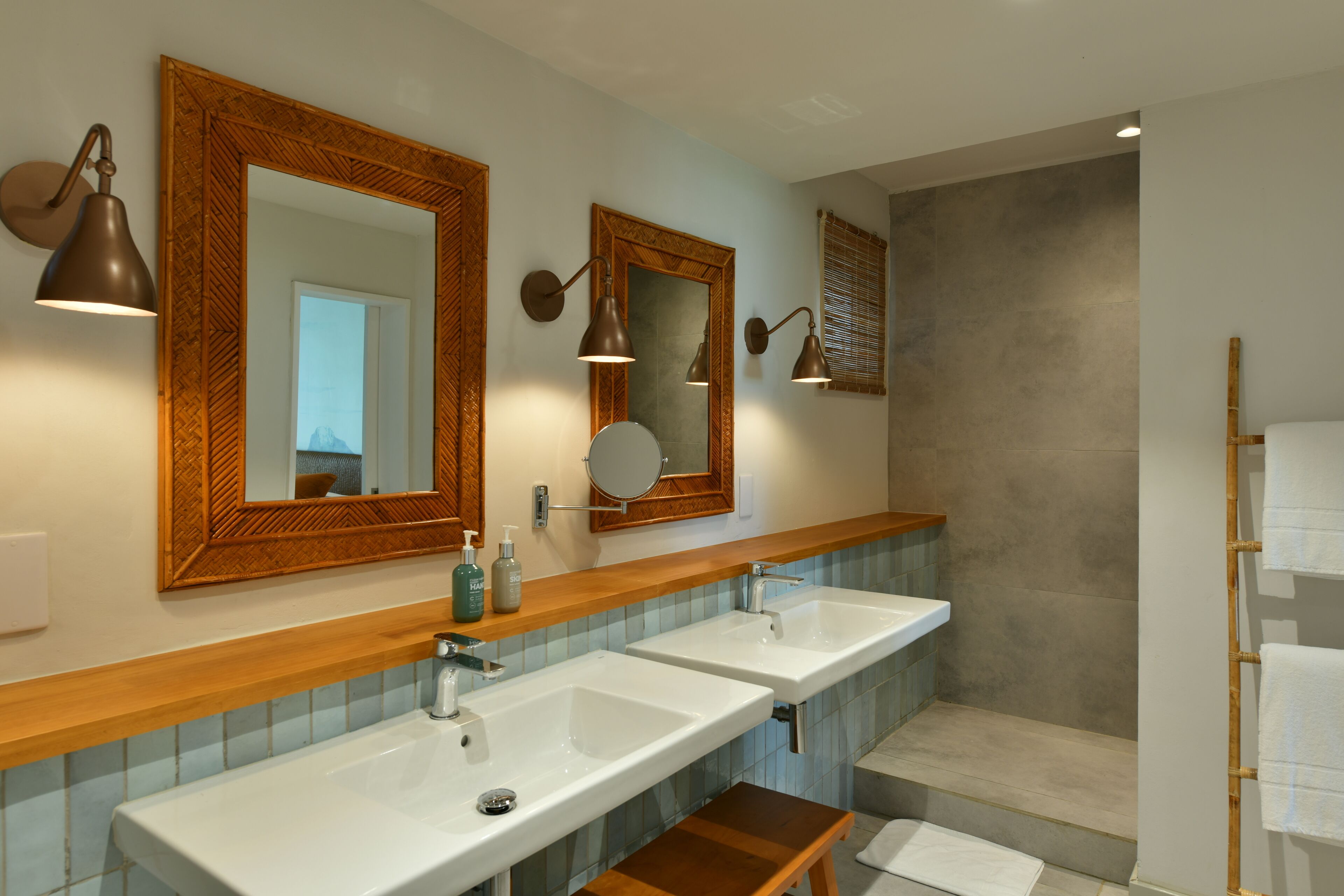 A modern bathroom with two sinks, wooden vanity, large mirrors, and wall-mounted lighting.