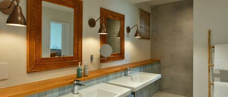 A modern bathroom with two sinks, wooden vanity, large mirrors, and wall-mounted lighting.