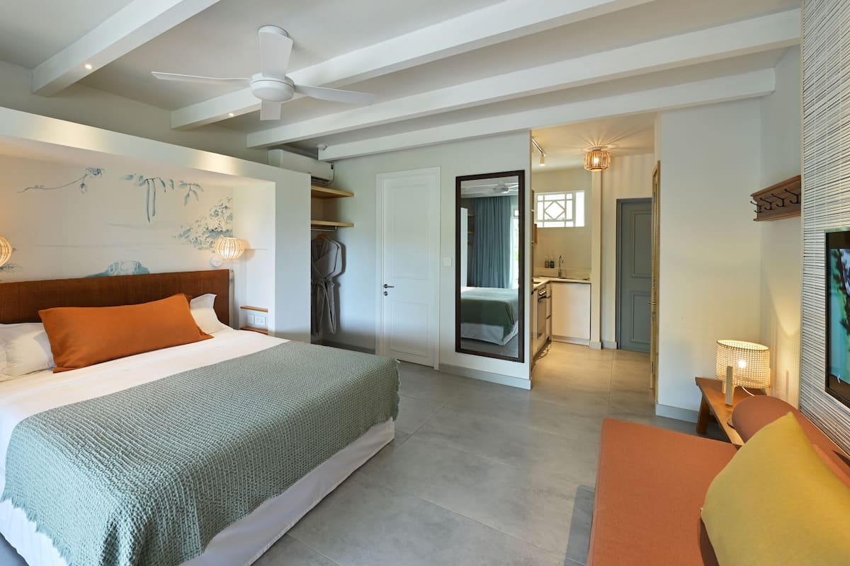 Een moderne hotelkamer met een groot bed, een plafondventilator, een kleine kitchenette en een badkamer zichtbaar door een open deur.