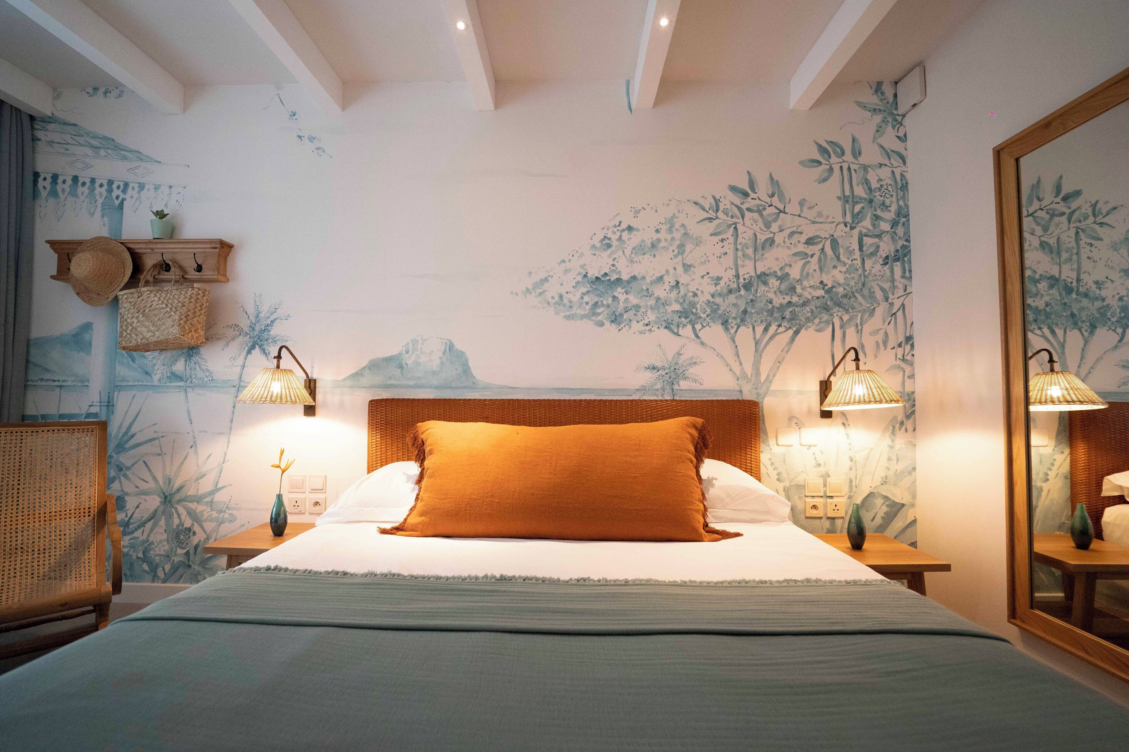 A bedroom with a large bed, two bedside lamps, a wooden headboard, and a wall mural.